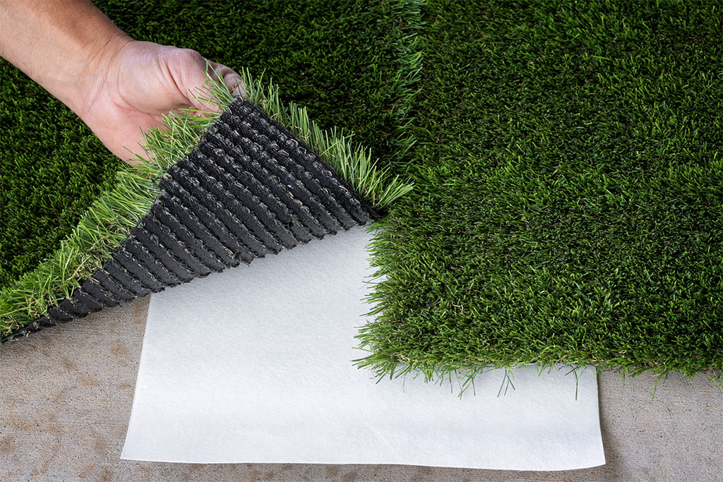 Hands putting artificial turf on top of seam tape