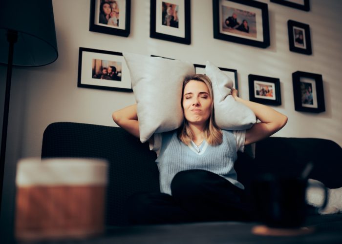 Woman,Sitting,On,A,Sofa,Covering,Her,Ears,With,Pillows.